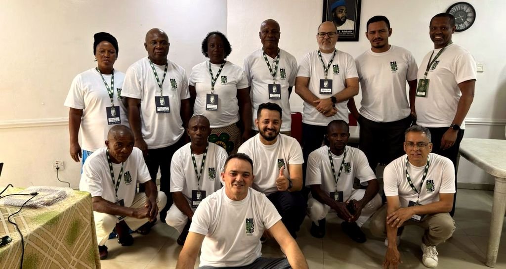 Grupo grande de irmãos nigerianos e visitantes brasileiros, uns em pé e outros agachados, sorrindo para a foto.